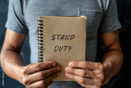 A man holds a notebook with the words Stamp duty. Taxes assessed during the transfer of real estate between two parties. Buying housing and land. Property. Stamp Duty Land Tax SDLT. photo
