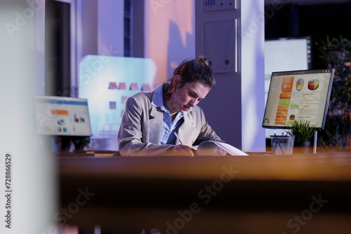 Entrepreneur looking at document with financial growth report while working overhours at investment plan to increase company profit. Businesswoman planning marketing strategy. Business concept
