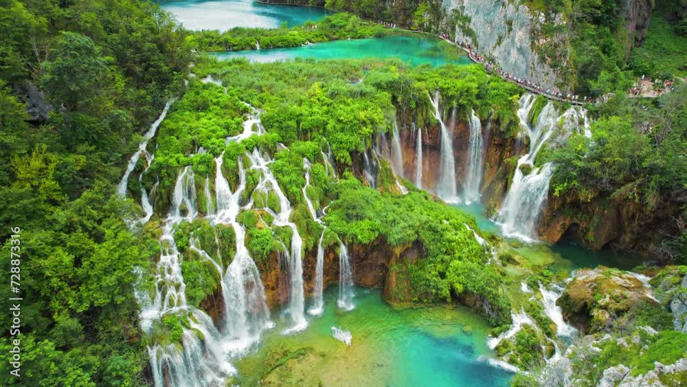 Crowd of tourists visit famous Plitvice waterfalls in Croatia. Mountain streams flow into a lake with azure clear water.