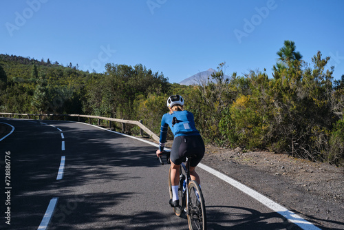 Woman cyclist riding a bicycle on the road. Attacking the climb. Effortful cycling mood. Cycle in beautiful nature. Woman cyclist wearing cycling kit and helmet. Tenerife, Canary Island, Spain.