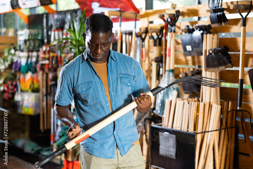 Focused adult african american man looking for pitchfork to work in his garden at gardening supply store photo