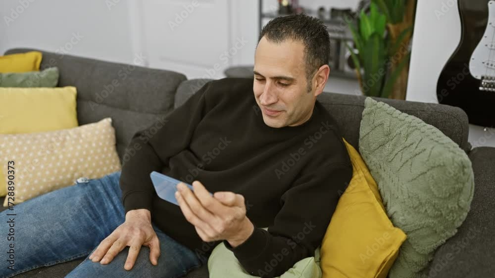 Smiling hispanic man using smartphone in cozy modern living room Smiling hispanic man using smartphone in cozy modern living room