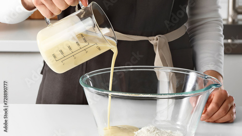 Closeup of man using a glass measuring cup to pour mixture in bowl with flour. (ID: 728890777)