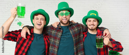 Happy young men with mugs of green beer on light background. St. Patrick's Day celebration
