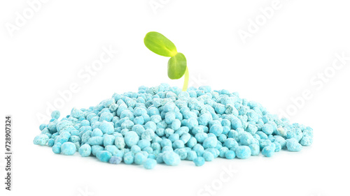Green seedling growing from pile of blue granular fertilizer on white background photo