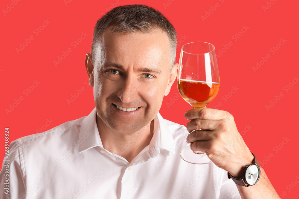 Mature man with glass of wine on red background, closeup