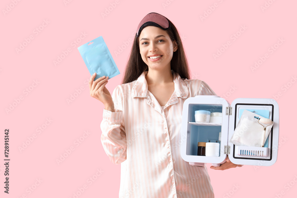 Beautiful young happy woman with facial mask and small refrigerator for cosmetic products on pink background Beautiful young happy woman with facial mask and small refrigerator for cosmetic products on pink background