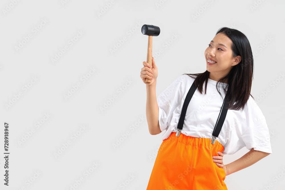 Asian woman in jumpsuit with hammer on white background Asian woman in jumpsuit with hammer on white background