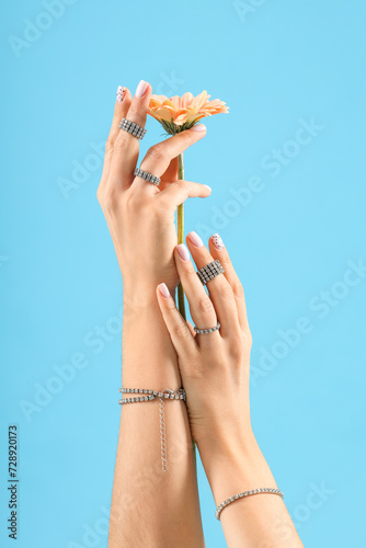 Hands of young woman with rings, bracelets and flower on blue background