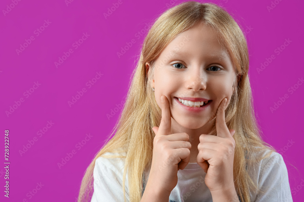 Happy little girl pointing at healthy teeth on purple background