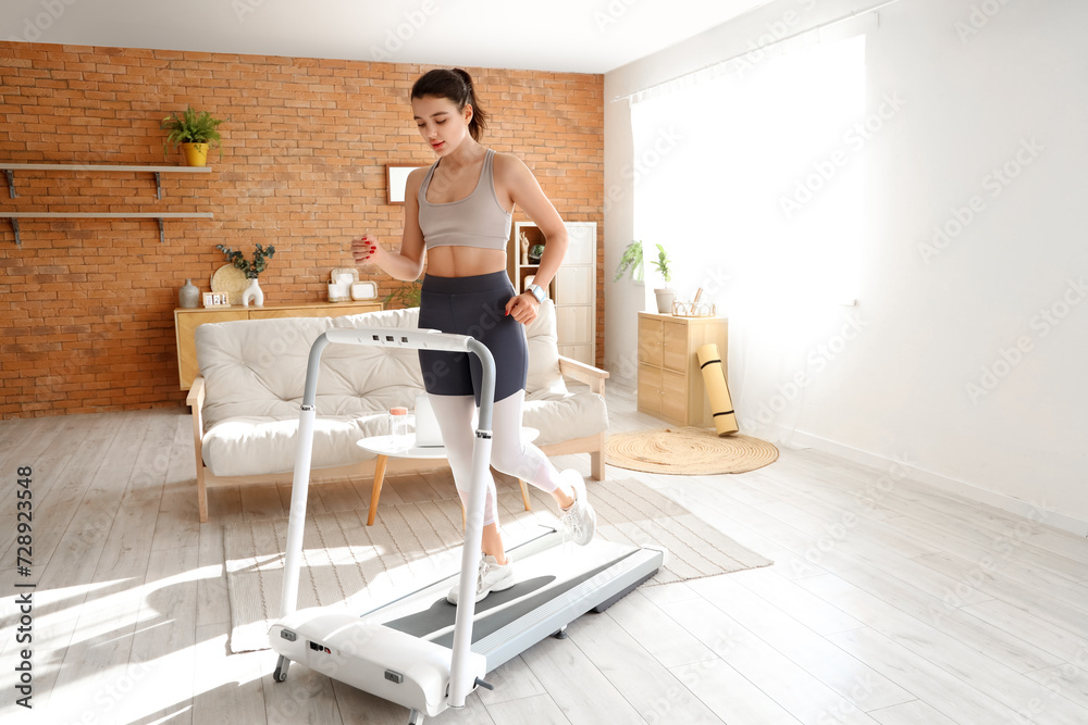 Sporty young woman exercising on treadmill at home