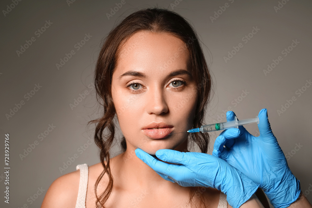 Beautiful young woman receiving lip injection on grey background Beautiful young woman receiving lip injection on grey background