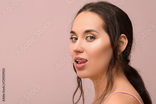 Beautiful young woman with natural makeup showing tongue on color background
