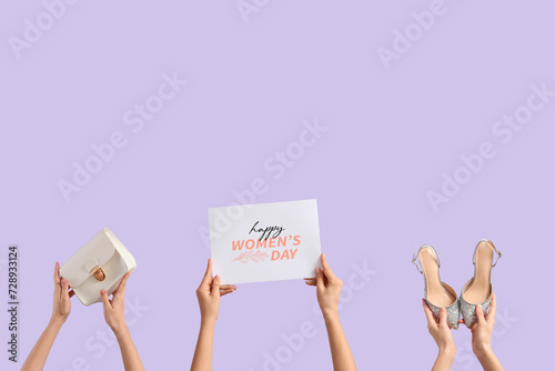 Female hands with festive postcard, handbag and high heel shoes on lilac background. International Women's Day celebration