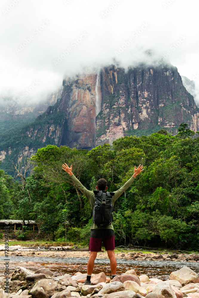 Obraz premium young adult person with backpack and arms raised looking at Angel Falls in Canaima National Park, Venezuela