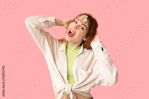 Beautiful young happy woman with paper fish attached to her forehead on pink background. April Fools Day celebration