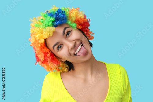 Beautiful young woman in funny clown disguise on blue background. April Fools Day celebration