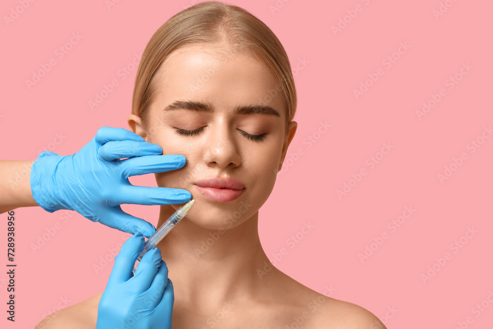 Young woman receiving filler injection in lips on pink background Young woman receiving filler injection in lips on pink background