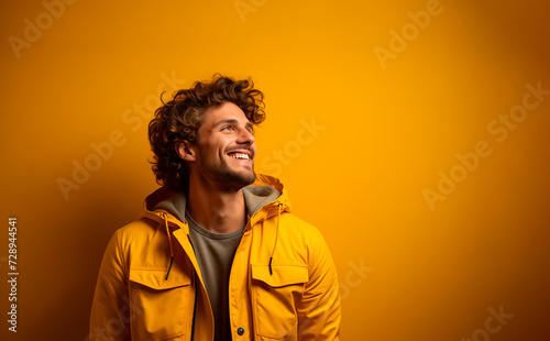 young man dressed in yellow looks to the side happy and smiling. scene with text space with yellow background