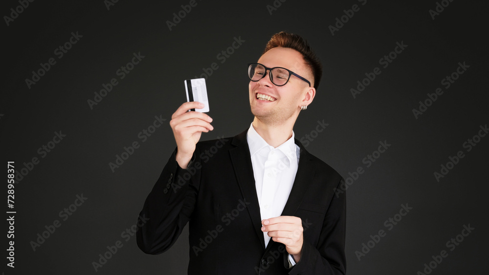 Banking service. Cashless payment. Satisfied smiling business man client holding credit card isolated on dark black empty space background. Banking service. Cashless payment. Satisfied smiling business man client holding credit card isolated on dark black empty space background.
