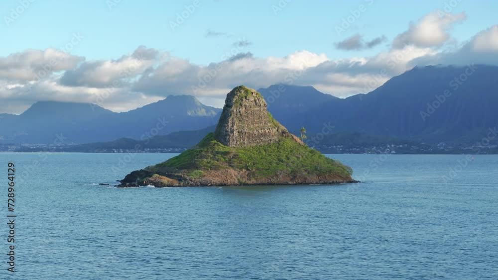 Scenic Oahu island nature Hawaii. Coconut palm trees on edge of Chinamans Hat island with Kualoa Ranch mountain on motion background. Pyramid shape Mokolii basalt island on background of cloudy sky Scenic Oahu island nature Hawaii. Coconut palm trees on edge of Chinamans Hat island with Kualoa Ranch mountain on motion background. Pyramid shape Mokolii basalt island on background of cloudy sky