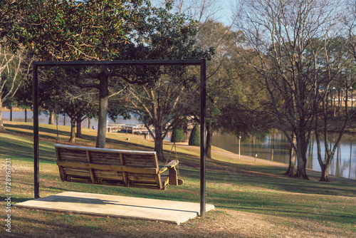 A rustic swing bench on a hill in a park with a scenic view of a lake in early spring at sunset
