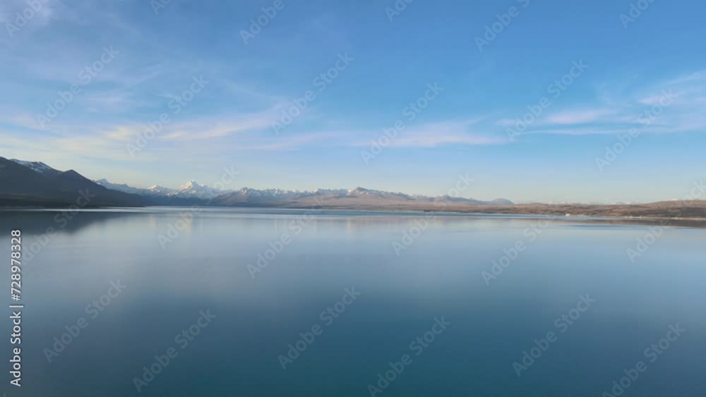 Panoramic aerial view of Lake Pukaki at sunset, surrounded by the Southern Alps, in New Zealand. Snow-capped peaks in the background.