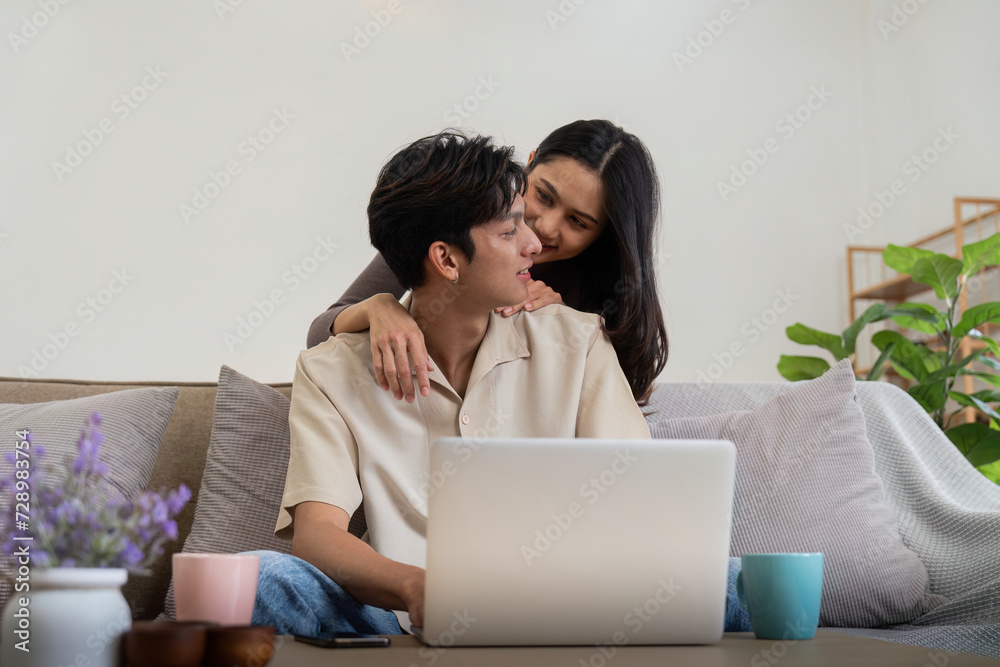 Young couple asian using laptop together while sitting on sofa at home Young couple asian using laptop together while sitting on sofa at home