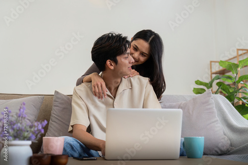 Young couple asian using laptop together while sitting on sofa at home