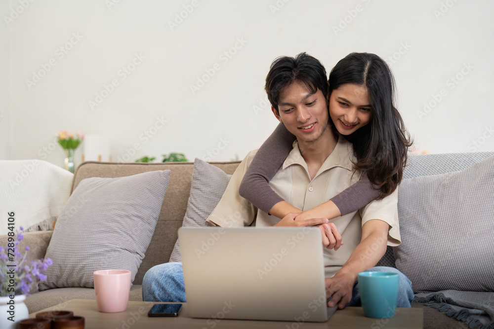 Young couple asian using laptop together while sitting on sofa at home Young couple asian using laptop together while sitting on sofa at home