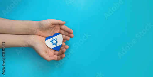 banner of a child's hands holding an Israeli flag in the shape of a heart. Concept of peace at home, conflict in Israel. child against war. blue background, copyspace
