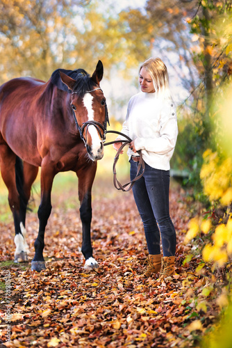 Young blonde girl with her horse walking through a colorful autumn forest. © RD-Fotografie