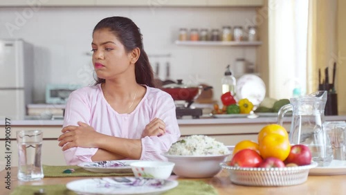 Indian woman on dining table waiting for husband or child after preparing food at home for lunch - concept of family caring, responsibility and patience photo
