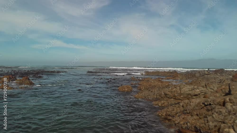 Drone flying low and fast between boulders onto sea front with bamboo covered waters as waves come in the perspective rises displaying open ocean on a partly cloudy day. Drone flying low and fast between boulders onto sea front with bamboo covered waters as waves come in the perspective rises displaying open ocean on a partly cloudy day.