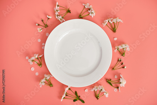 White plate and branches of cherry blossoms on pink background, top view, copy space.