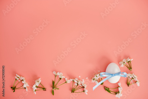White flowers and an egg with a blue ribbon on a pink background. Easter background, a place to copy. Flat lay