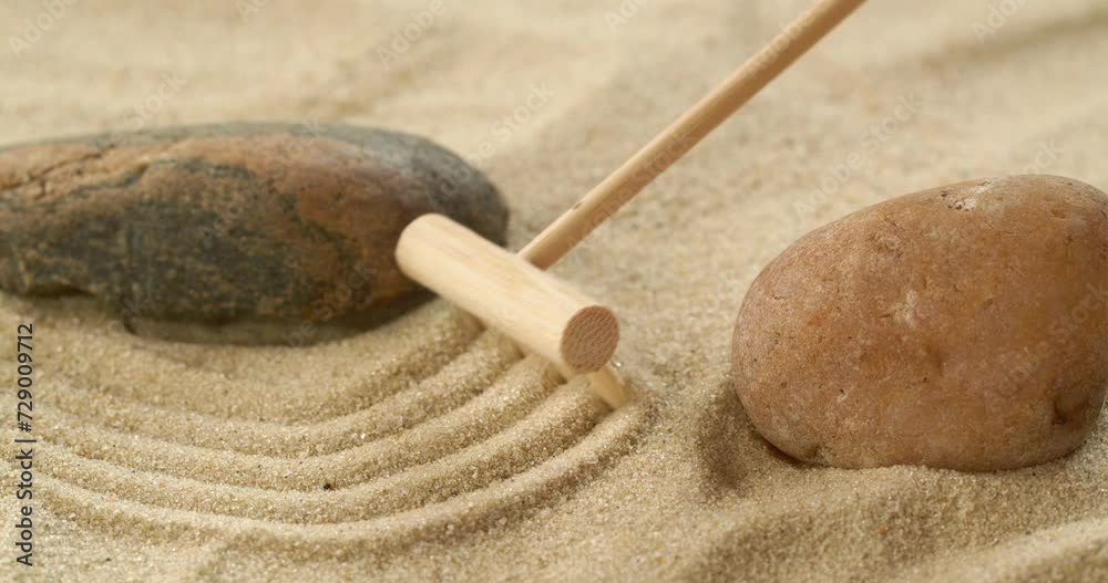 Close-up making zen garden with sand and stones using mini bamboo wooden rake