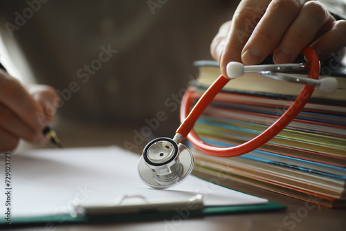 Male doctor search information in book and writtnig prescription, medical stethoscope on the desk at clinic. Medical knowledge and education concept.