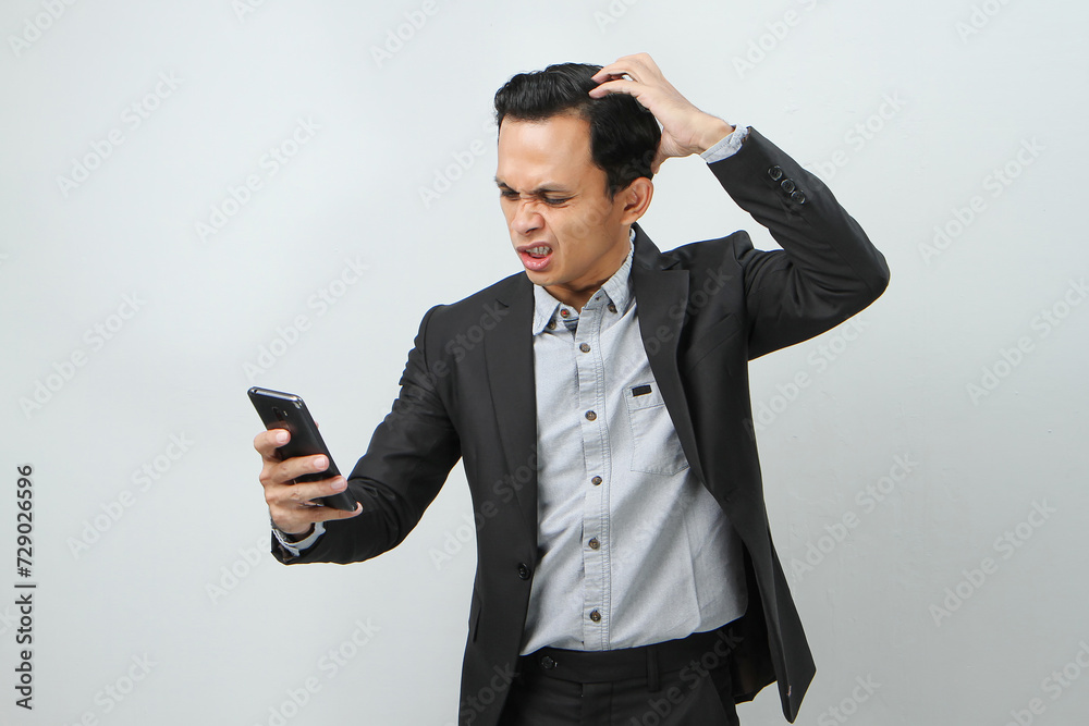 angry mad asian indonesian business man in suit holding smart phone on isolated background angry mad asian indonesian business man in suit holding smart phone on isolated background