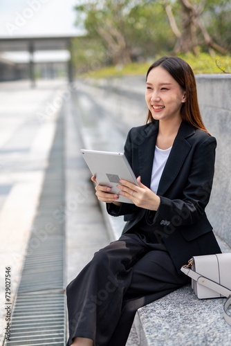 Asian woman sitting and using tablet outdoor, enjoying a moment of break from office © asean studio