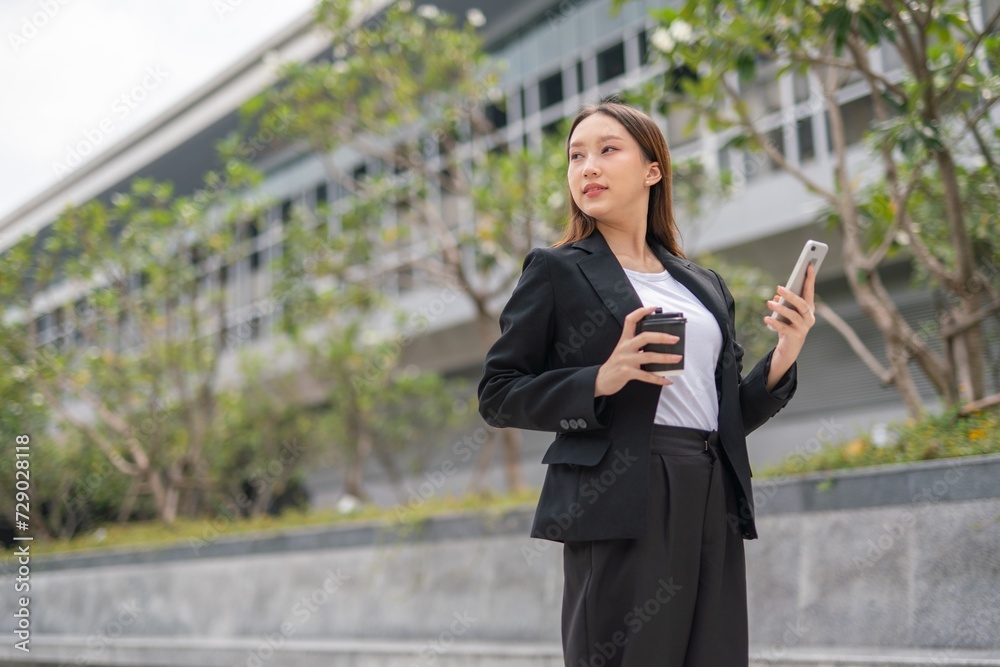 Young Asian Woman holding coffee cup and using phone outdoor in a central business district area Young Asian Woman holding coffee cup and using phone outdoor in a central business district area