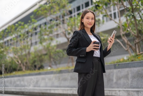 Young Asian Woman holding coffee cup and using phone outdoor in a central business district area