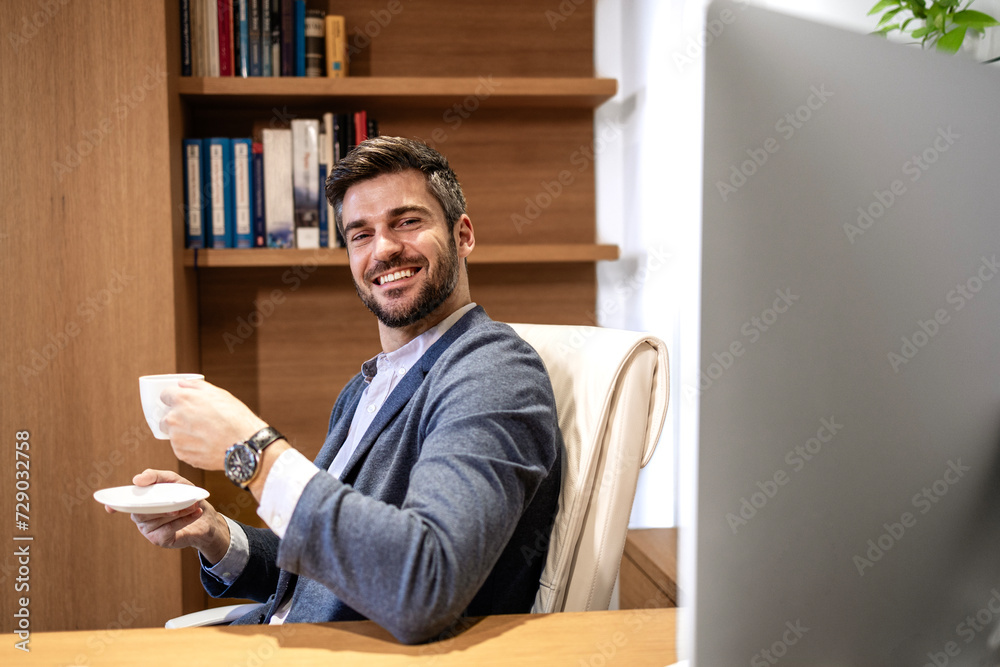 Handsome director in business suit looking to the camera and holding cup of coffee.