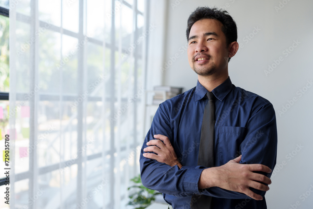 Young Asian businessman stands with his arms crossed, smiling happily. It's refreshing to work in a financial business. Independent entrepreneur Goals of successful business in the office. Young Asian businessman stands with his arms crossed, smiling happily. It's refreshing to work in a financial business. Independent entrepreneur Goals of successful business in the office.