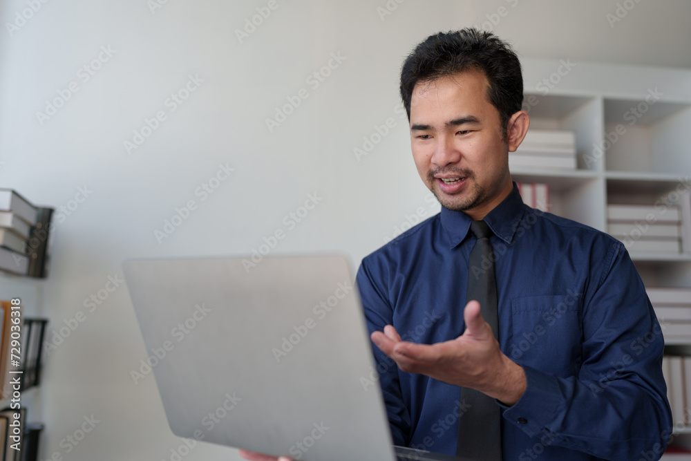Young Asian businessman stands holding a laptop. Open your hands to show a presentation. Explain detailed information about investing in online financial businesses to the team according to goals.