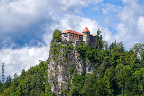 Scenic view of castle on top of rock with Slovenian flag waving at lakeshore of Slovenian Lake Bled on a cloudy summer day. Photo taken August 8th  2023  Bled  Slovenia.