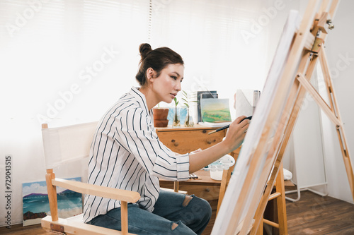 Portrait photo of young beautiful Asian woman artist painting water color art picture in indoor studio.