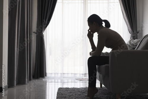 Silhouette of a person suffering from depression in the house, Depressed woman sitting alone on the Sofa feel stress, sad and worried in the dark room. person are stressed. photo