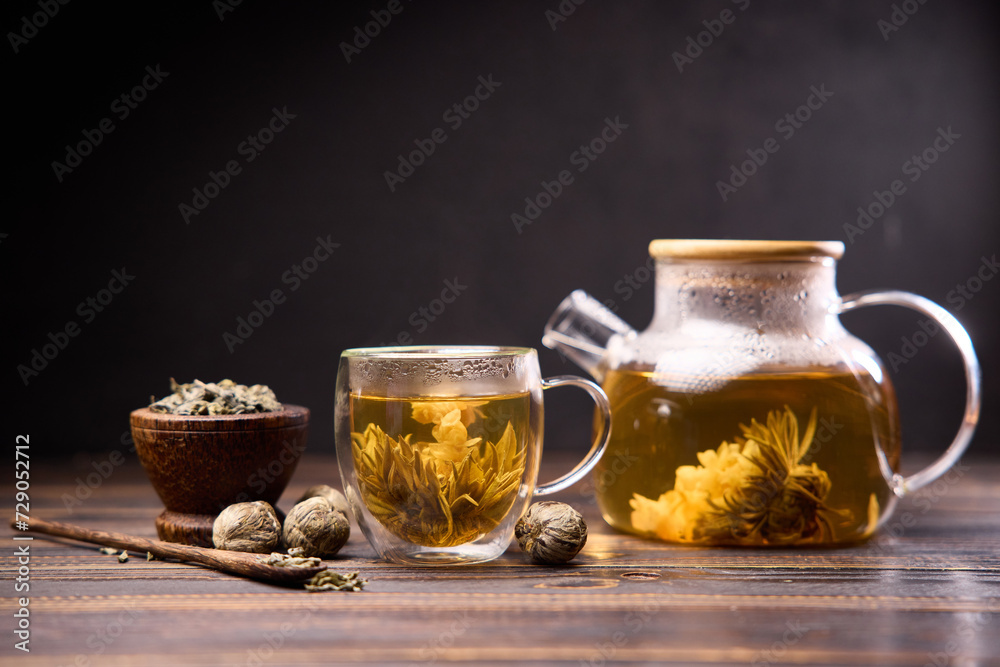 Teapot and glass cup with blooming tea flower inside on a wooden table Teapot and glass cup with blooming tea flower inside on a wooden table