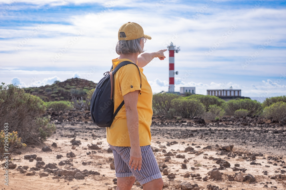 Rear view of a carefree mature woman in yellow enjoying outdoor activity looking at the lighthouse. Weekend tourism and outdoor recreation, lifestyle concept.